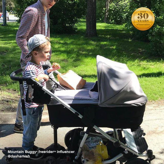 family strolling through park with toddler riding their freerider™ scooter board attached to rear of duet™ double buggy - Mountain Buggy freerider™ influencer @dashamish
