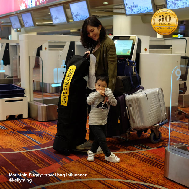 madre con niño pequeño en el aeropuerto con equipaje - Mountain Buggy travel bag  influencer @kellynting