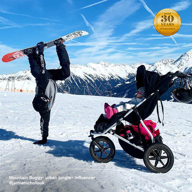 active family visiting snowy mountains as toddler keeps warm riding in mountain buggy urban jungle all-terrain buggy with sleeping bag - urban jungle™ influencer @jamienichollsuk